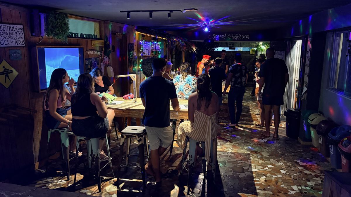 Bar do hostel à noite com hóspedes nas mesas altas